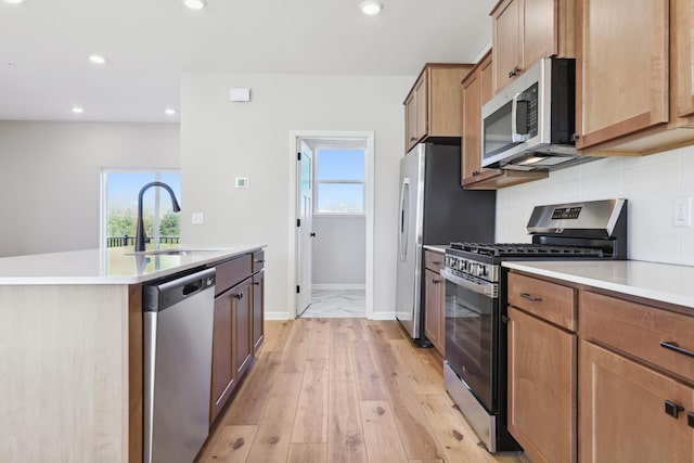 kitchen featuring stainless steel appliances, backsplash, light wood-style flooring, a sink, and an island with sink