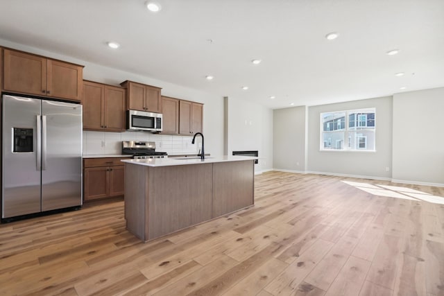 kitchen with stainless steel appliances, a sink, backsplash, and light wood-style flooring