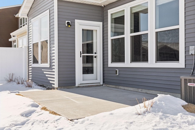 snow covered property entrance with a patio, cooling unit, and fence