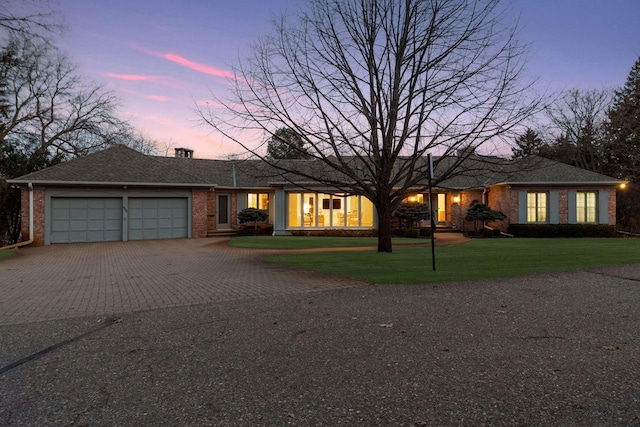 ranch-style home featuring brick siding, an attached garage, decorative driveway, and a front lawn