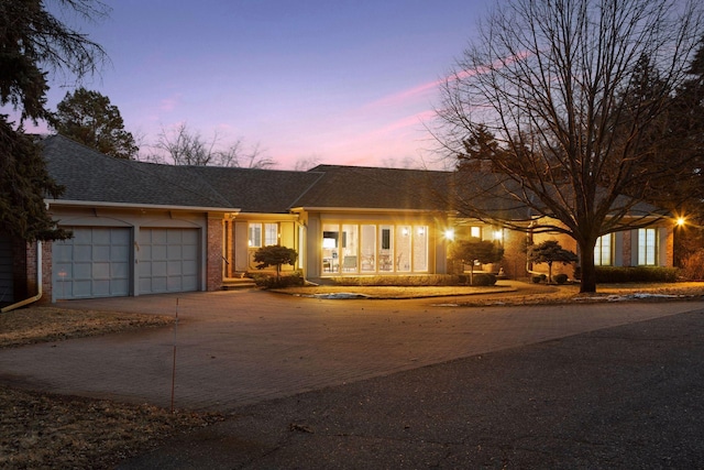 ranch-style house featuring decorative driveway, brick siding, a garage, and a shingled roof