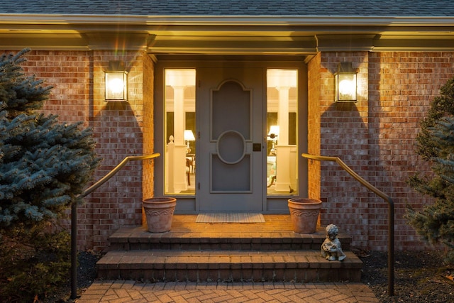 doorway to property featuring brick siding, covered porch, and roof with shingles