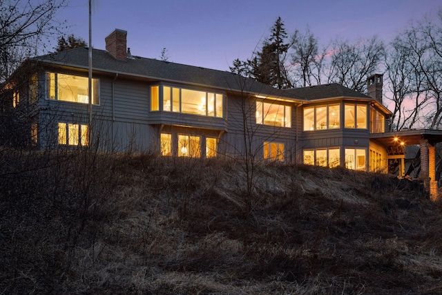 back of property at dusk featuring a chimney and roof with shingles