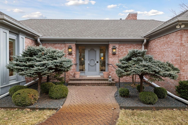 view of exterior entry featuring brick siding, roof with shingles, and a chimney