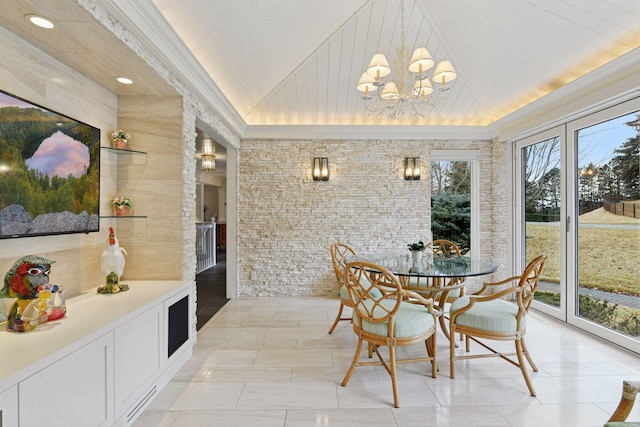 dining area featuring a notable chandelier, ornamental molding, brick wall, and vaulted ceiling