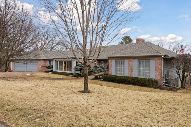 ranch-style house with a front yard, an attached garage, a shingled roof, a chimney, and brick siding