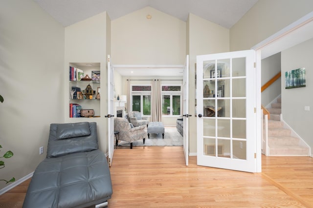 sitting room with high vaulted ceiling, wood finished floors, stairway, french doors, and a fireplace