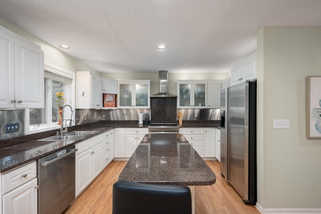 kitchen featuring white cabinetry, wall chimney exhaust hood, appliances with stainless steel finishes, and a sink