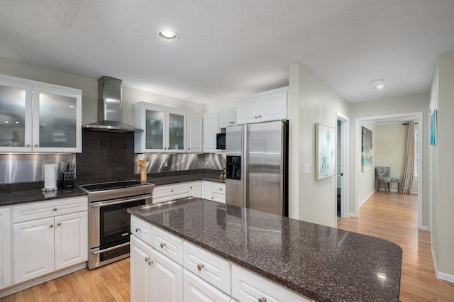 kitchen featuring stainless steel appliances, light wood finished floors, white cabinets, and wall chimney range hood