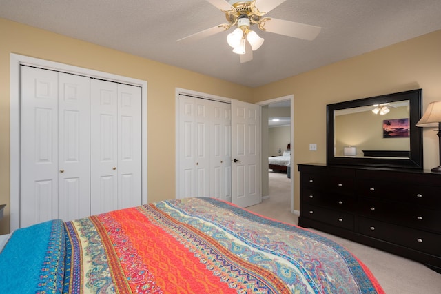 bedroom with light carpet, a textured ceiling, two closets, and a ceiling fan