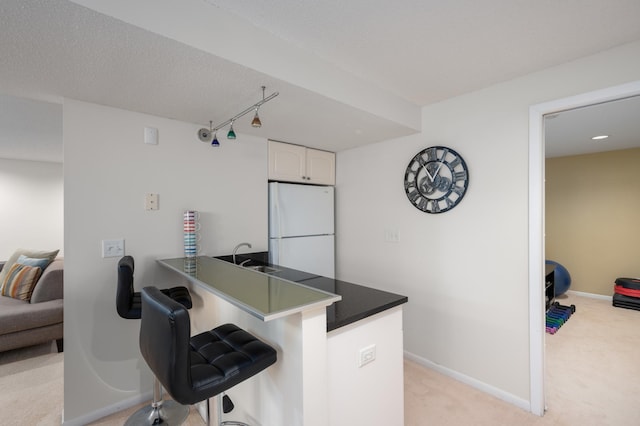 kitchen with a peninsula, freestanding refrigerator, white cabinets, a kitchen bar, and light colored carpet