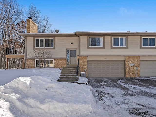 raised ranch with entry steps, brick siding, a chimney, and an attached garage