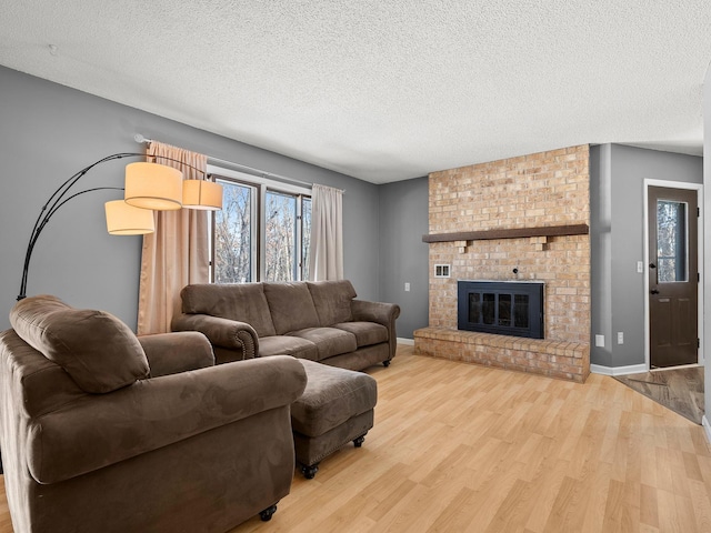 living room featuring a textured ceiling, a fireplace, baseboards, and light wood-style floors