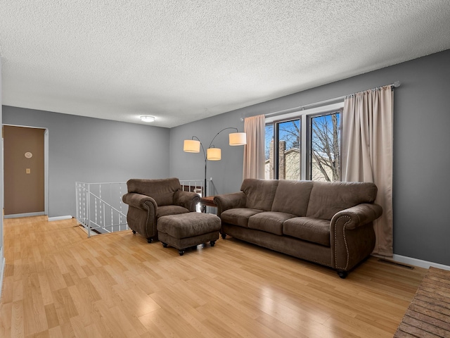 living area featuring light wood-style floors, baseboards, visible vents, and a textured ceiling