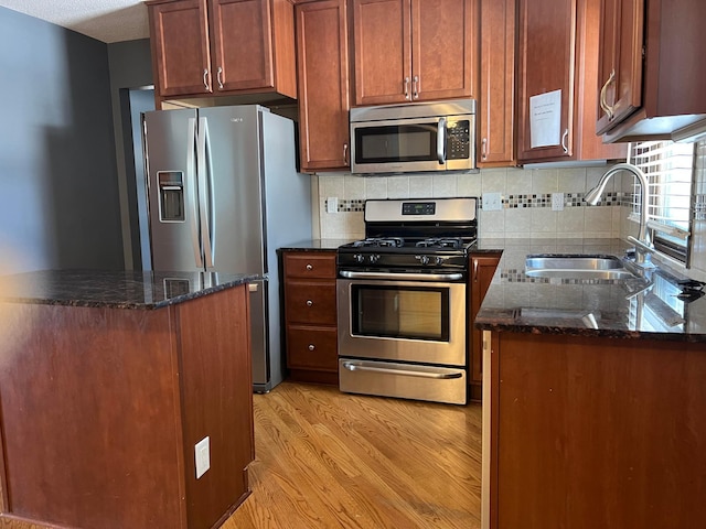 kitchen with a sink, dark stone countertops, appliances with stainless steel finishes, light wood finished floors, and decorative backsplash