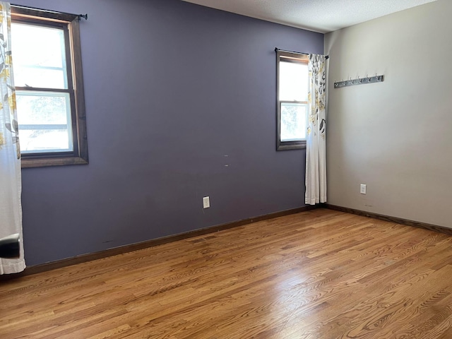 empty room featuring a textured ceiling, baseboards, and wood finished floors