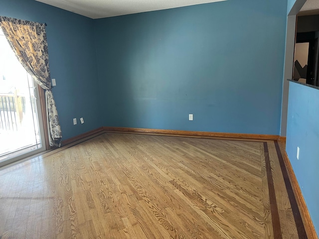 spare room with baseboards and wood finished floors