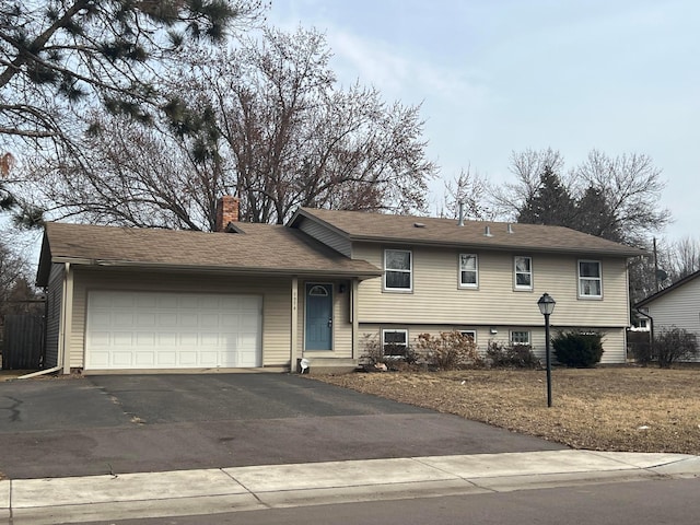 split level home featuring a chimney, an attached garage, and aphalt driveway
