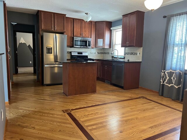 kitchen with wood finished floors, dark countertops, tasteful backsplash, a sink, and appliances with stainless steel finishes