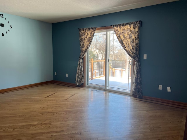 spare room with baseboards, a textured ceiling, wood finished floors, and visible vents