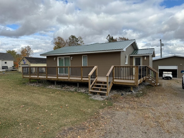 rear view of house with an outbuilding, a detached garage, a lawn, metal roof, and a wooden deck