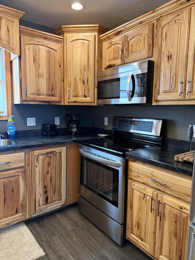 kitchen featuring stainless steel appliances, dark wood-style flooring, dark countertops, and a sink