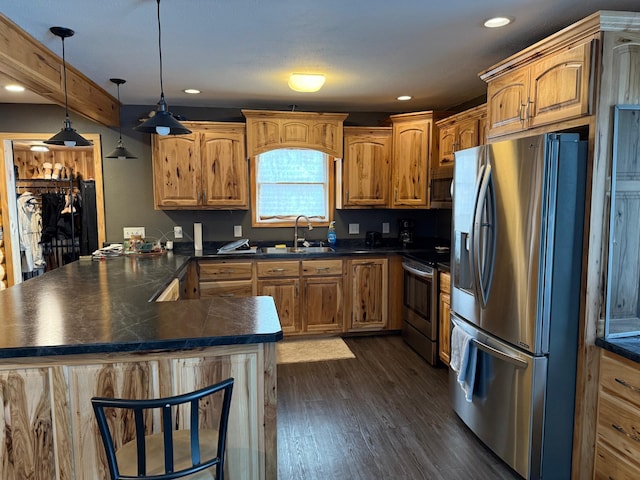 kitchen with dark wood finished floors, dark countertops, a peninsula, stainless steel appliances, and a sink