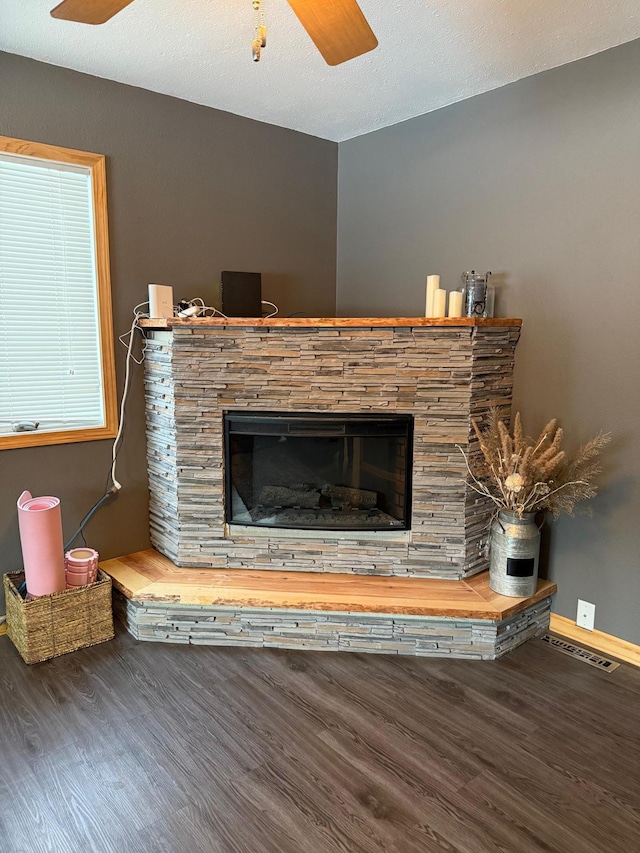 interior details with ceiling fan, a textured ceiling, a stone fireplace, wood finished floors, and visible vents