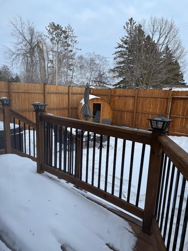 snow covered deck with a fenced backyard