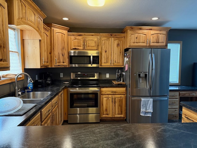 kitchen featuring recessed lighting, stainless steel appliances, a sink, brown cabinetry, and dark countertops