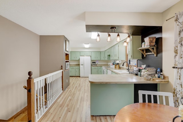 kitchen featuring a peninsula, a sink, green cabinets, light wood-type flooring, and white fridge with ice dispenser