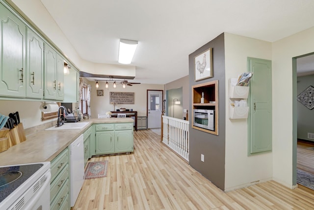 kitchen featuring white appliances, light wood-style flooring, a peninsula, green cabinets, and a sink