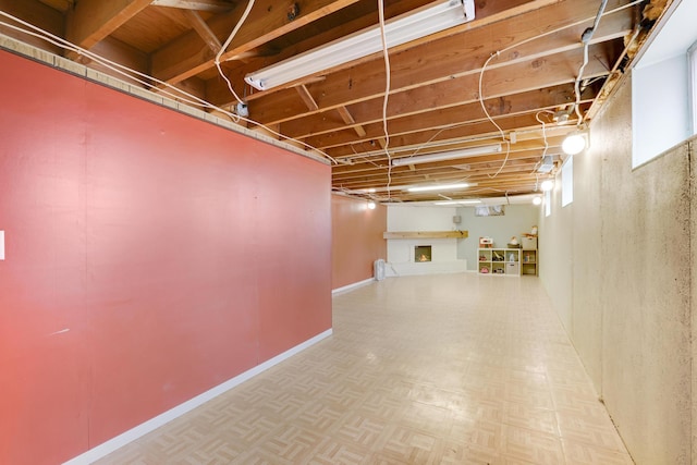 unfinished basement featuring a brick fireplace and baseboards