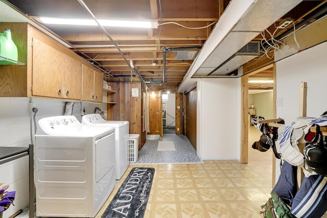 clothes washing area featuring light floors, wood walls, cabinet space, and washing machine and clothes dryer