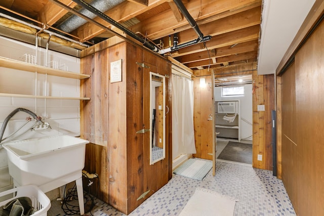 basement with a wall mounted AC, a sink, and wooden walls