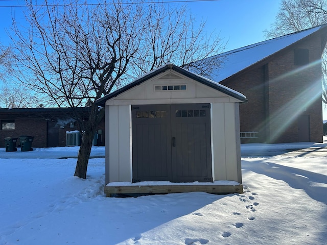 snow covered structure featuring an outbuilding and a shed