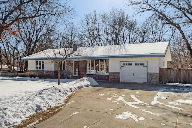 single story home with stucco siding, an attached garage, fence, stone siding, and driveway