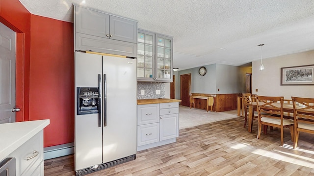 kitchen with pendant lighting, light wood-style flooring, glass insert cabinets, butcher block countertops, and stainless steel fridge with ice dispenser