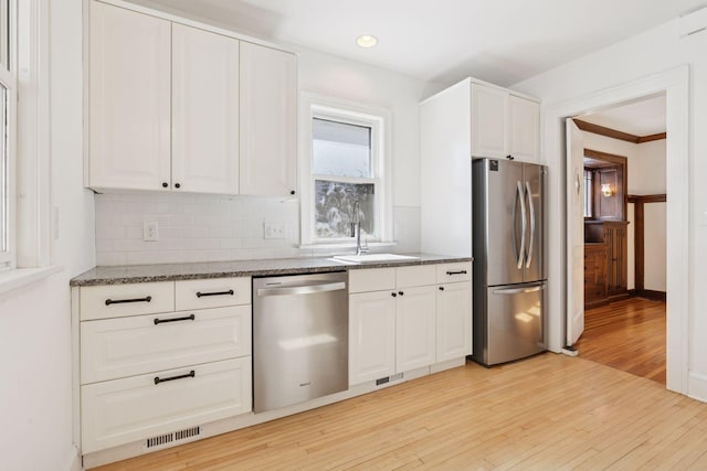 kitchen featuring light wood finished floors, visible vents, dark stone counters, appliances with stainless steel finishes, and a sink