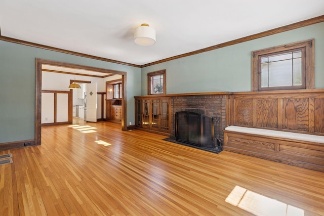 unfurnished living room featuring ornamental molding, a brick fireplace, light wood-style flooring, and baseboards