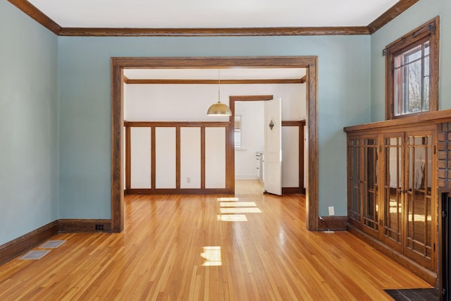 unfurnished room with visible vents, crown molding, light wood-style flooring, and baseboards