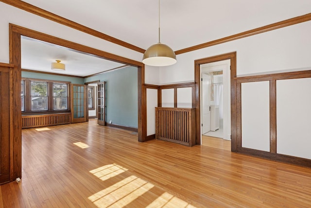 unfurnished living room with light wood-type flooring, baseboards, crown molding, and radiator heating unit