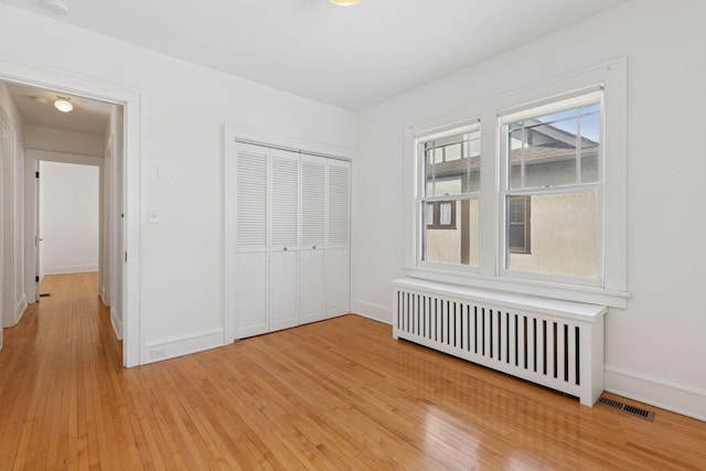 unfurnished bedroom with radiator heating unit, light wood-type flooring, visible vents, and baseboards