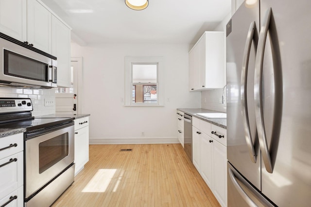 kitchen featuring stainless steel appliances, tasteful backsplash, light wood-type flooring, and visible vents