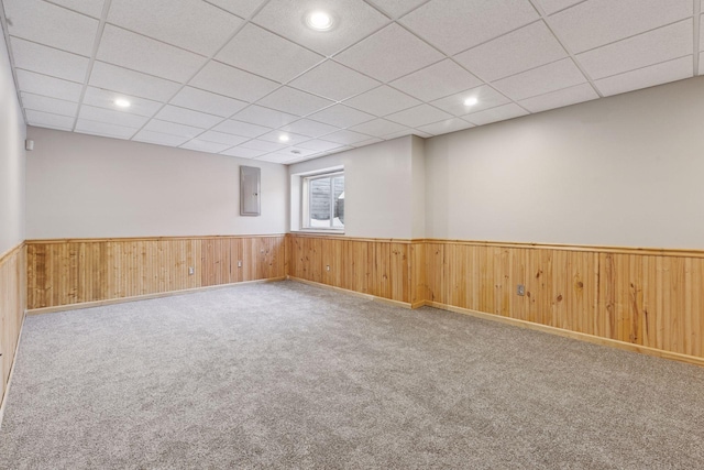 carpeted spare room with electric panel, a drop ceiling, wainscoting, and wood walls