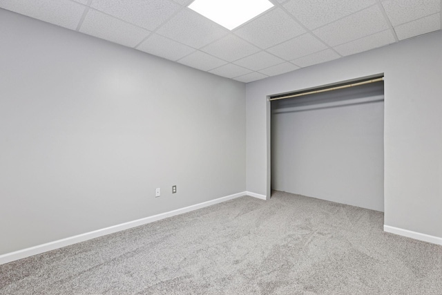 unfurnished bedroom featuring a closet, a drop ceiling, baseboards, and carpet