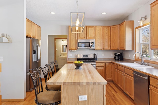 kitchen with light wood finished floors, wooden counters, a breakfast bar, stainless steel appliances, and a sink