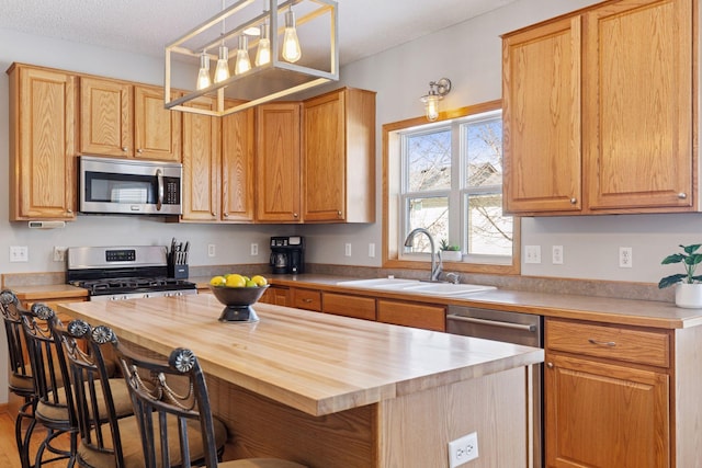 kitchen featuring a kitchen bar, a sink, wood counters, a kitchen island, and appliances with stainless steel finishes