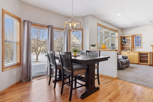 dining space featuring light wood finished floors, a chandelier, a textured ceiling, and baseboards