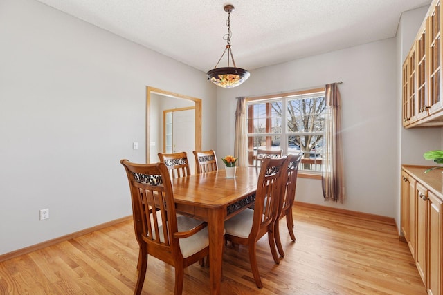 dining space featuring light wood-style flooring, a textured ceiling, and baseboards